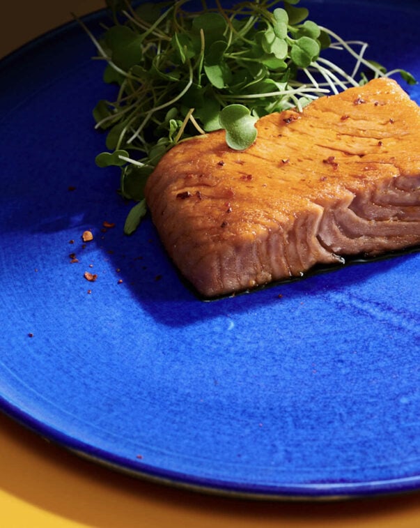 An alternative protein salmon filet on a blue plate with a side of greens.  photo courtesy of oshi.