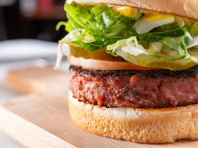 A closeup view of a plated plant-based burger with lettuce, tomatoes, and pickles