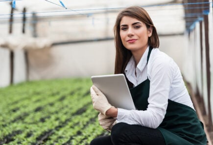 Female researcher in an indoor growing facility kneeling in front of rows of crops